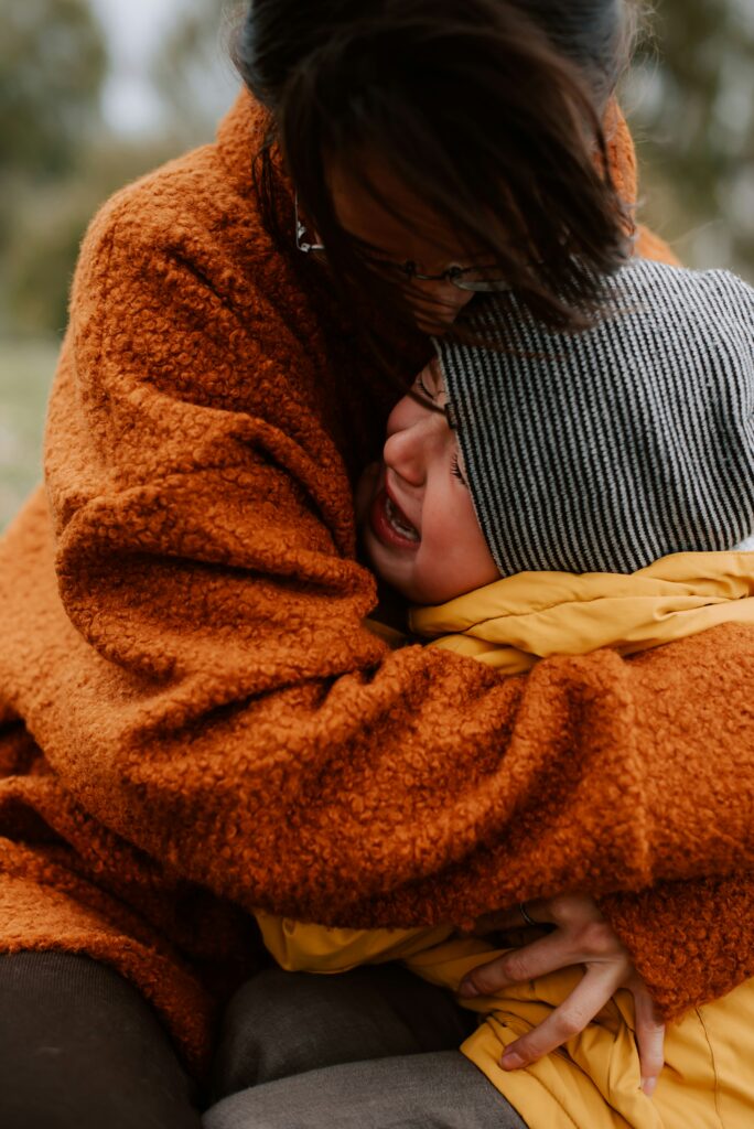 A mother kneeling to console her upset child, gently holding them in a comforting embrace.